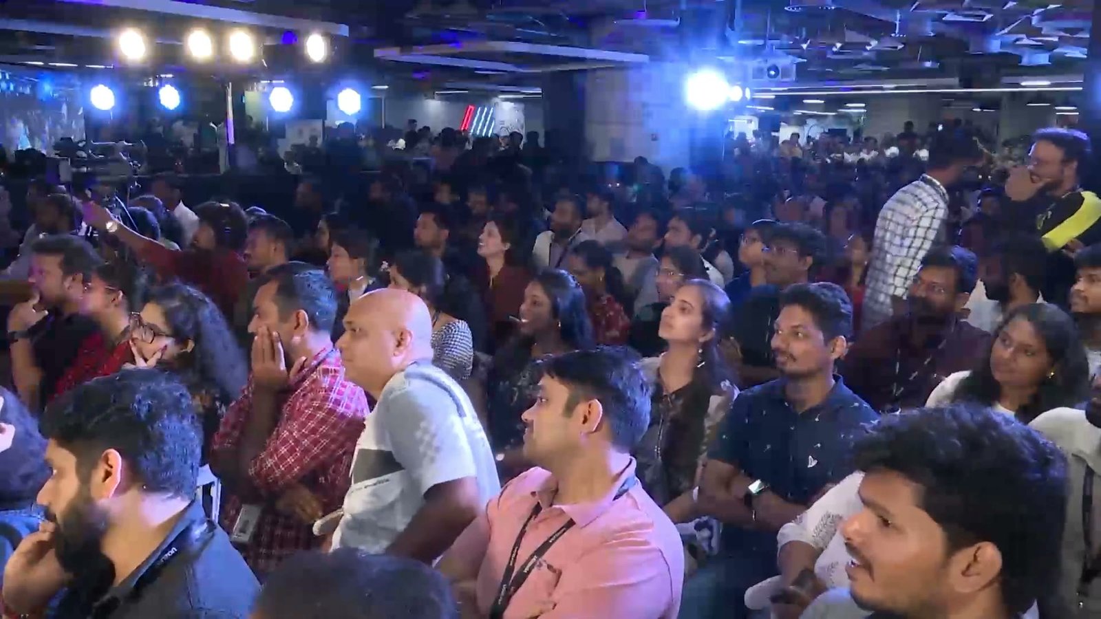 A packed hall of several hundred employees seated under stage lighting at a corporate celebration