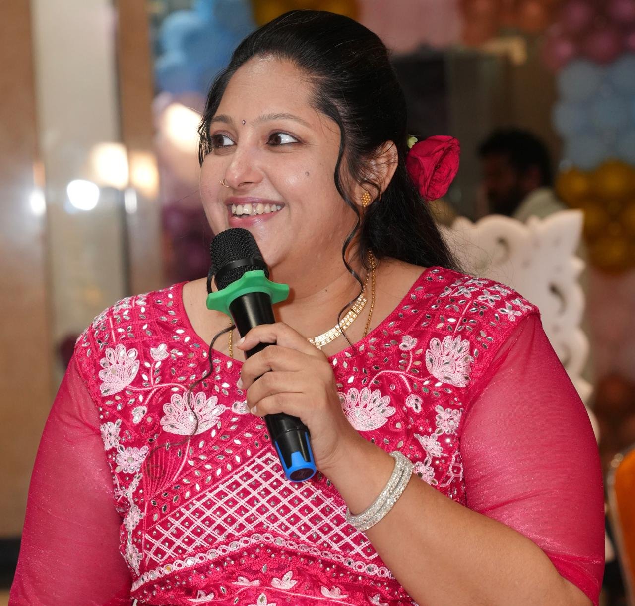 Close-up of Pooja Aravalapalli mid-address, smiling, microphone in hand