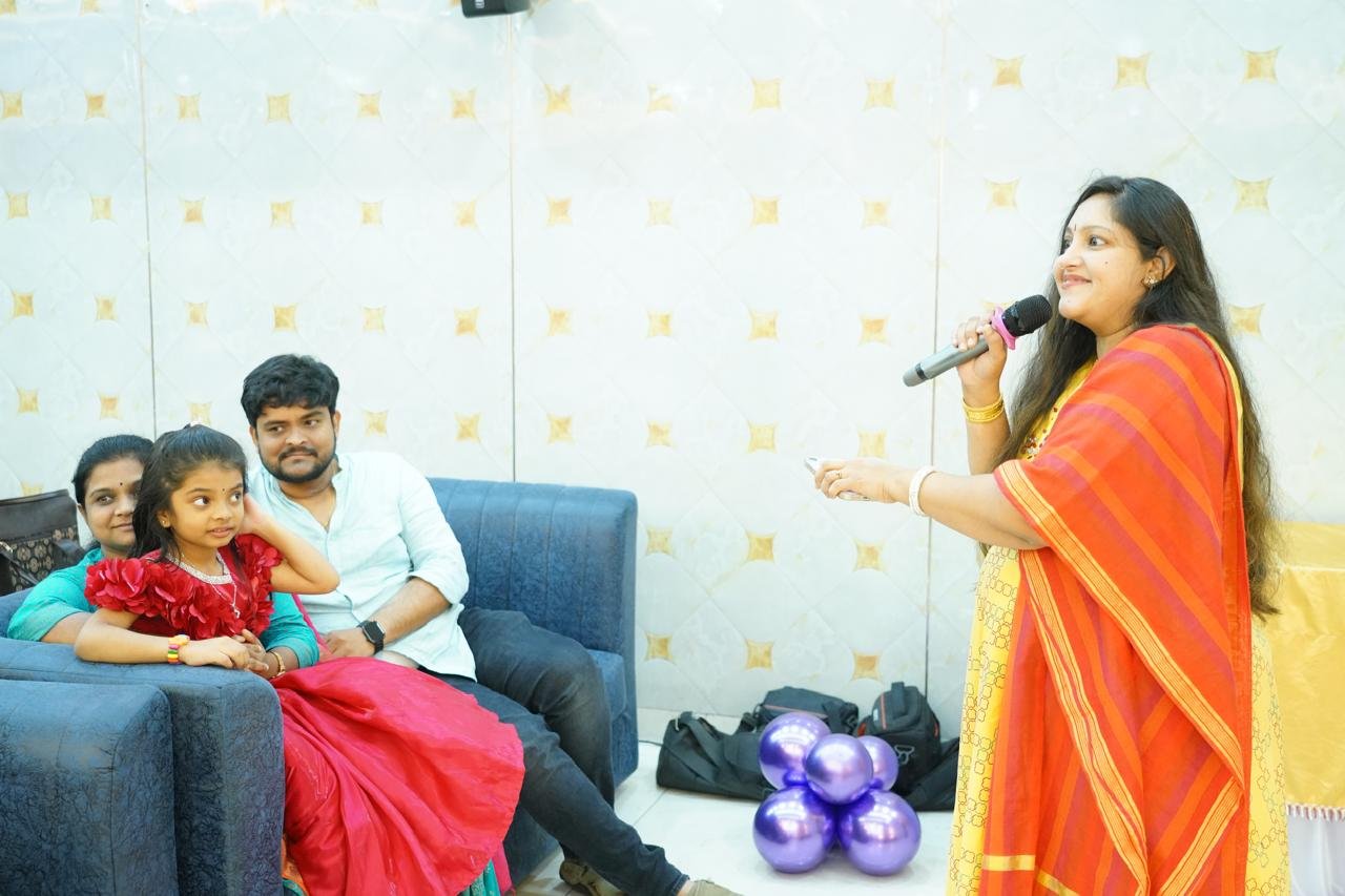Pooja Aravalapalli anchoring a family celebration, addressing a family seated together