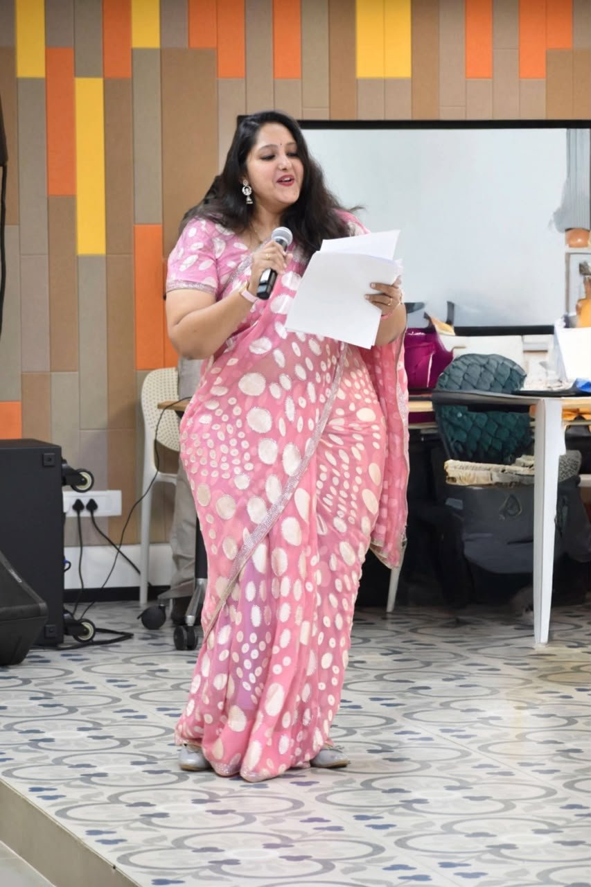 Pooja Aravalapalli anchoring an office event, reading from a run sheet with a microphone in hand