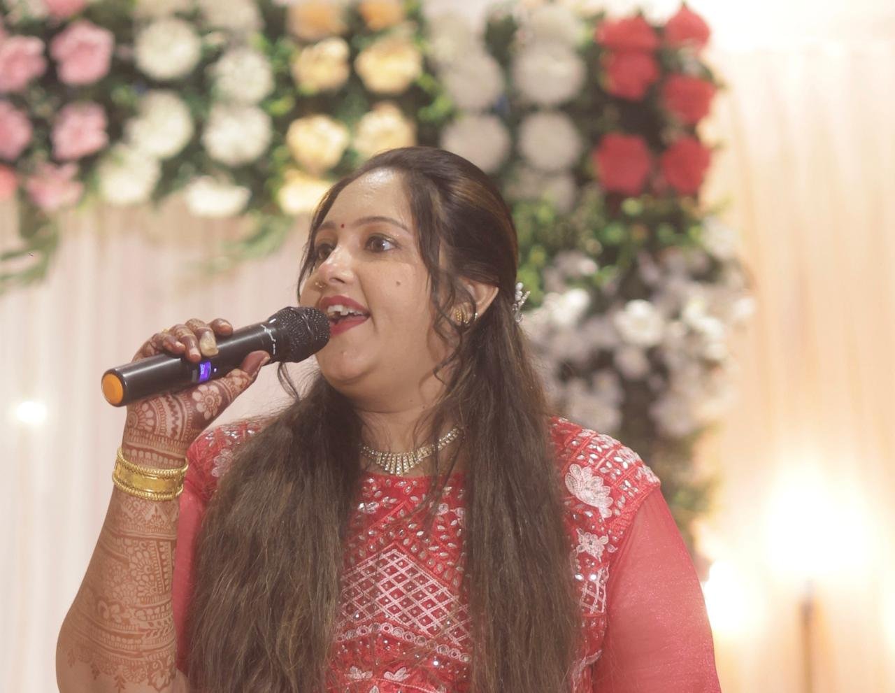Pooja Aravalapalli announcing at a wedding reception in front of a floral backdrop